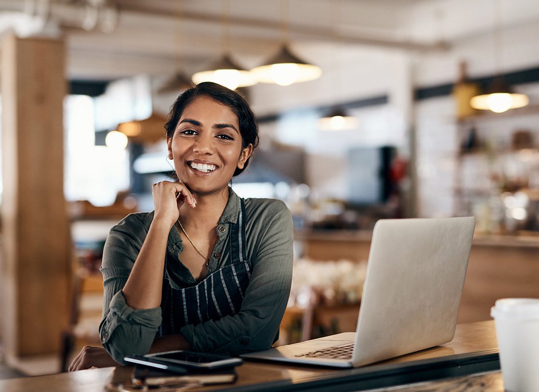 Contact - Portrait of a Cheerful Young Female Small Business Owner Working on her Laptop in a Cafe