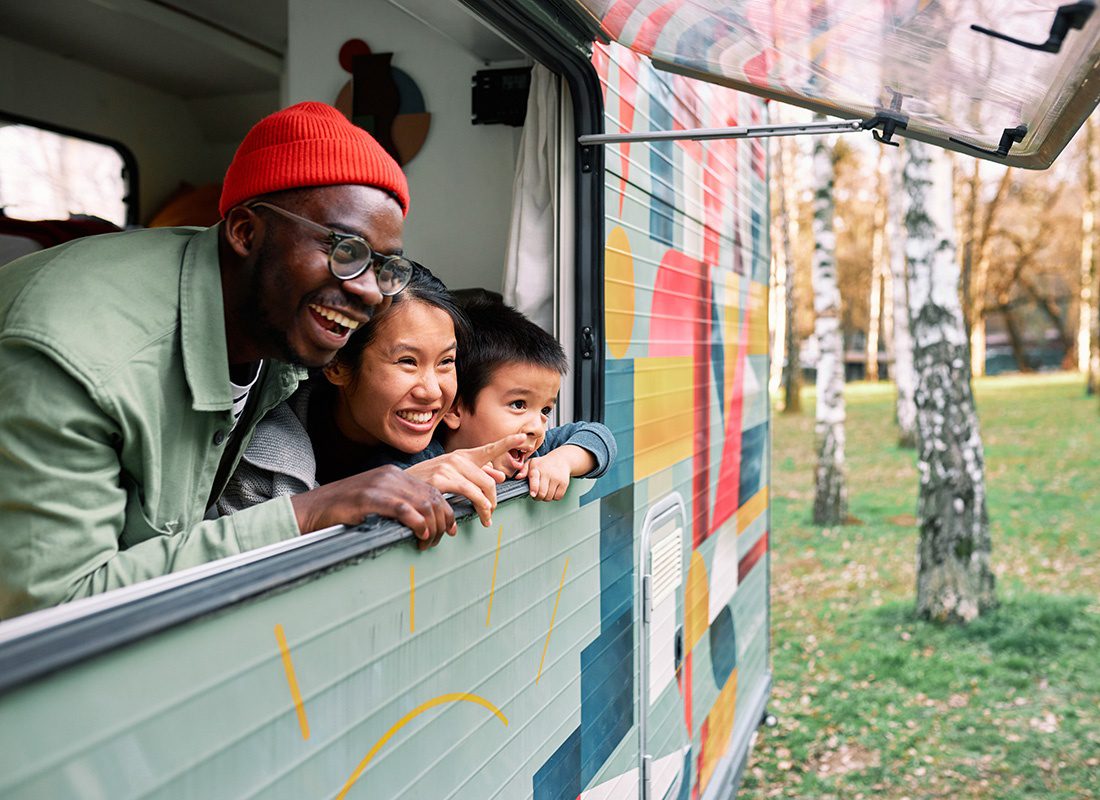 Personal Insurance - Portrait of an Excited Family with a Son Looking Out the Window in their Colorful RV Enjoying the View of the Forest